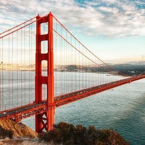 Una vista panoramica del Golden Gate Bridge che attraversa l'acqua, con lo skyline della città in lontananza sotto un cielo parzialmente nuvoloso.