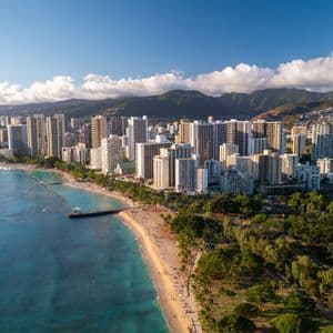 Una vista aerea dello skyline di una città lungo una spiaggia sabbiosa e un oceano turchese, con lussureggianti montagne verdi sullo sfondo.