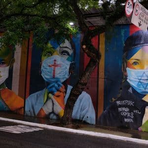Un colorido mural de arte callejero representa a tres niños con mascarillas decoradas con símbolos religiosos de diferentes fes.