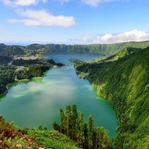 Vue aérienne de deux grands lacs de cratère connectés, entourés de pentes verdoyantes et escarpées, sous un ciel bleu nuageux.