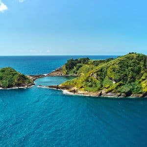 Un petit îlot volcanique vert avec un lagon central se trouve dans un vaste océan bleu sous un ciel clair.