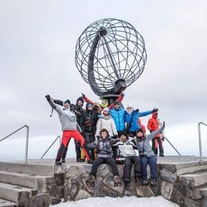 Un groupe WeRoad en tenue d'hiver posant devant une grande sculpture de globe métallique sur une plateforme de pierre enneigée.
