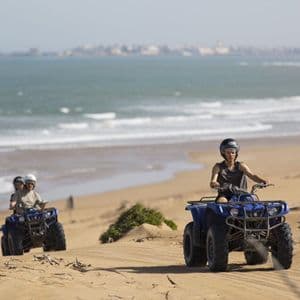 A WeRoad group trip riding quad bikes on sand dunes along a beach with the ocean in the background.