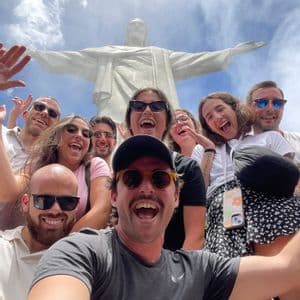 Un viaggio di gruppo WeRoad scatta un selfie sorridente con la statua del Cristo Redentore sullo sfondo.