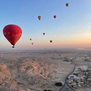 Muchos globos aerostáticos flotan sobre un pueblo desértico y colinas rocosas contra un cielo al amanecer.