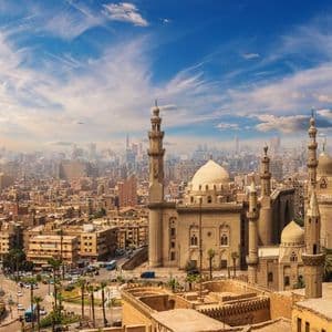 Una vista panorámica de una mezquita histórica con minaretes y cúpulas sobre un extenso y brumoso paisaje urbano bajo un cielo azul.