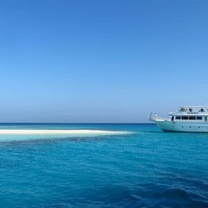 Un viaje en grupo de WeRoad en un gran barco blanco anclado en agua turquesa junto a un banco de arena blanca bajo un cielo azul claro.
