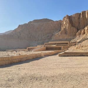 Un gran templo aterrazado con rampas y columnatas, construido en la base de un acantilado escarpado y rocoso en un paisaje desértico.