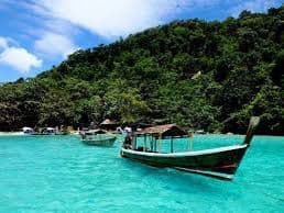 Dos botes de cola larga de madera flotan en agua turquesa frente a una exuberante isla cubierta de árboles bajo un cielo parcialmente nublado.