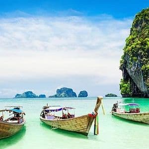 Varias barcas de cola larga amarradas en aguas turquesas poco profundas con una gran isla rocosa cubierta de vegetación de fondo.