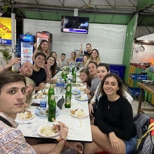 Un gruppo WeRoad a cena in un ristorante locale, seduto a un lungo tavolo e sorridendo alla macchina fotografica.