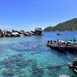 Un viaggio di gruppo WeRoad su barche long-tail in una baia con acqua turchese cristallina e costa rocciosa.