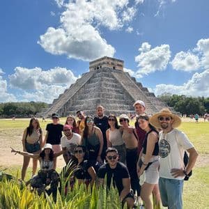 A WeRoad group trip posing and cheering for a photo in front of a large stone pyramid under a clear blue sky.