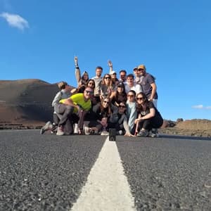 Un viaggio di gruppo WeRoad in posa per una foto su una strada deserta, con colline scure e un cielo azzurro chiaro sullo sfondo.