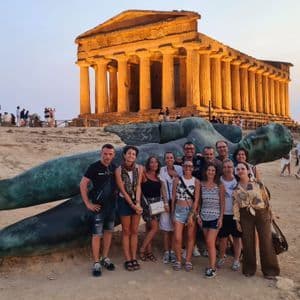 Un grupo de viaje de WeRoad posa para una foto frente a una gran estatua caída con un templo antiguo al fondo al atardecer.