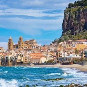 Un pueblo costero con una catedral, enclavado al pie de un gran acantilado, junto a una playa de arena con olas.