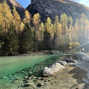 Un viaggio di gruppo WeRoad sulla riva di un lago limpido e turchese, ai piedi di una montagna soleggiata e di una foresta autunnale.