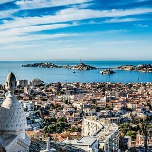 Una vista panorámica desde arriba de una ciudad costera con tejados de tejas rojas, con vistas a un mar azul con varias islas bajo un cielo brillante.