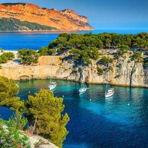 Varios veleros anclados en una cala apartada con agua turquesa, rodeada de acantilados cubiertos de árboles bajo un cielo azul claro.