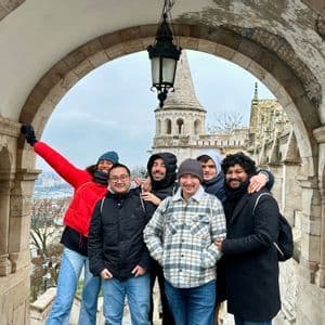 Un voyage de groupe WeRoad de six personnes posant sous une arche en pierre avec une tourelle de château visible en arrière-plan.