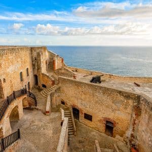 Una fortaleza de piedra histórica con cañones en sus murallas con vistas al mar bajo un cielo azul parcialmente nublado.