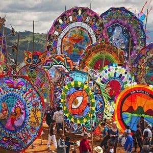 Aquiloni giganti, colorati e finemente dipinti sono esposti a una folla durante un festival all'aperto, con colline sullo sfondo.