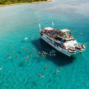 Veduta aerea di un viaggio di gruppo WeRoad su una barca per feste, con persone che nuotano in acqua limpida e turchese.