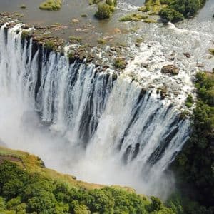 Una vista aerea di un'enorme cascata che precipita da un'ampia scogliera rocciosa in un baratro nebbioso circondato da una lussureggiante foresta verde.