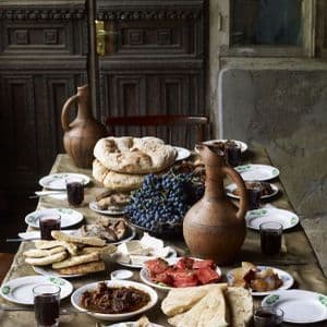 Una tavola imbandita con un banchetto tradizionale di pane azzimo, uva, formaggio, carne e vino in brocche di argilla.