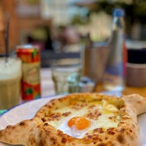 Un pane a forma di barca ripieno di formaggio fuso e un uovo all'occhio di bue, su un piatto su un tavolo all'aperto.