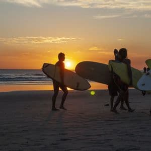 Surfistas de WeRoad silueteados en la playa al atardecer con sus tablas.