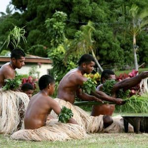 Un gruppo di uomini, in gonne d'erba tradizionali e bracciali di foglie, esegue una cerimonia all'aperto attorno a una ciotola di legno.