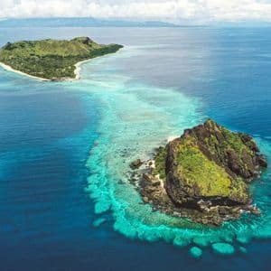 Una vista aerea di due isole lussureggianti e verdi, una grande e una piccola, circondate da barriere coralline turchesi e dall'oceano blu profondo.