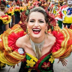 Una donna con un vivace costume rosso e giallo e maniche a balze sorride ampiamente durante una sfilata di carnevale.