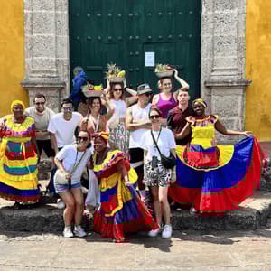 Un gruppo di viaggio WeRoad posa per una foto su gradini di pietra con donne che indossano abiti tradizionali colorati di fronte a un edificio giallo.