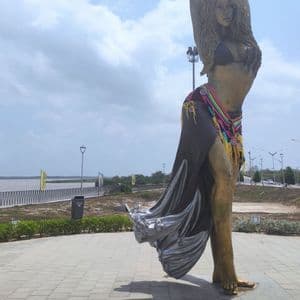 Un'alta statua di bronzo di Shakira in posa danzante si erge su una passeggiata lungofiume lastricata sotto un cielo nuvoloso.