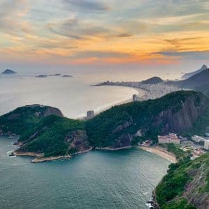 Una vista panoramica di una città costiera con una spiaggia a mezzaluna, circondata da montagne verdi e dal mare al tramonto.