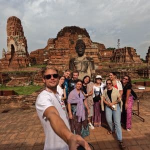Un uomo si scatta un selfie con un gruppo WeRoad davanti a una grande statua di Buddha e rovine di templi antichi.