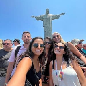 Eine WeRoad-Gruppenreise macht an einem sonnigen Tag ein lächelndes Selfie vor der Christus-Erlöser-Statue.