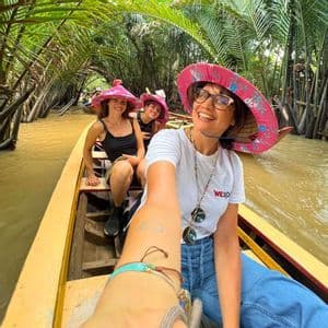 Eine WeRoad-Gruppe von Frauen mit pinkfarbenen Spitzhüten macht ein Selfie auf einem Boot in einem von Palmen gesäumten Kanal.