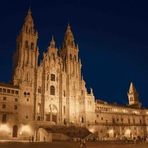 Una majestuosa y ornamentada catedral con intrincadas agujas, iluminada por luces cálidas bajo un cielo nocturno azul oscuro.