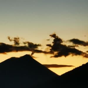 Deux sommets de montagne se profilent sur un ciel jaune et bleu au crépuscule, avec quelques nuages sombres au-dessus.