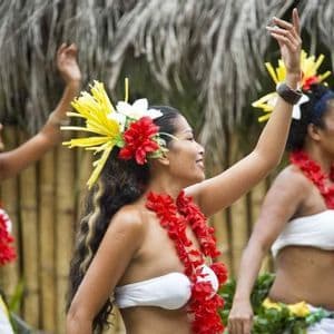 Tre donne di profilo eseguono una danza tradizionale, indossando ghirlande di fiori rossi e copricapi floreali colorati.