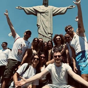 Un viaje en grupo de WeRoad sonríe y posa para una foto frente a la estatua del Cristo Redentor bajo un cielo azul claro.