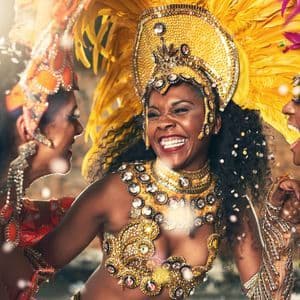 Trois femmes en costumes de carnaval élaborés et garnis de plumes rient et dansent ensemble sous une pluie de confettis.