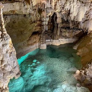 A pool of turquoise water illuminated from below inside a cavern filled with stalactites and stalagmites.