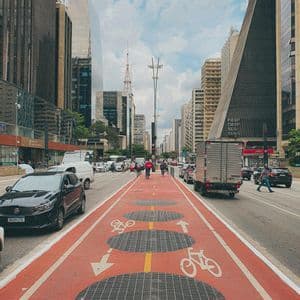 Un carril bici ancho y rojo con símbolos de bicicleta recorre el centro de una ajetreada calle urbana flanqueada por rascacielos.