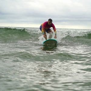 Un hombre con una camiseta de licra colorida surfea una pequeña ola en el océano bajo un cielo nublado.
