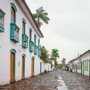 Una calle adoquinada mojada flanqueada por edificios coloniales encalados con puertas, ventanas y balcones coloridos bajo un cielo cubierto.