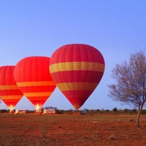 Drei rote und gelbe Heißluftballons bereiten sich bei Sonnenaufgang in einer Reihe über einer Wüstenlandschaft auf den Start vor.